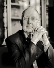 Black and white portrait of an older man with glasses, thoughtfully posed.