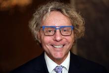 Headshot of a man with curly hair and blue glasses, smiling.