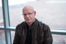 Headshot of a middle-aged man with glasses, wearing a brown leather jacket.