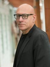 Headshot of bald man wearing glasses and a black blazer.