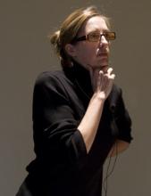 Thoughtful woman in black turtleneck, hand to chin.