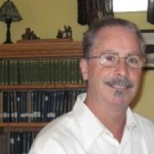 Headshot of a man with glasses, smiling gently.
