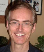Headshot of a man with glasses, smiling.