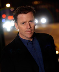 Headshot of a man, possibly in his 40s, wearing a dark jacket and blue shirt.