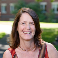 Headshot of a smiling woman with shoulder-length brown hair, wearing a rust-colored sleeveless top.