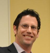 Headshot of a man, smiling, wearing glasses and a suit jacket.