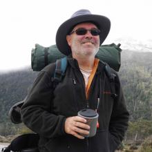 Smiling hiker with backpack enjoying a beverage in a mountain landscape.