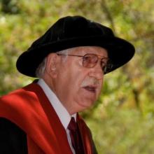 Elderly Karl Popper in academic regalia, speaking outdoors.